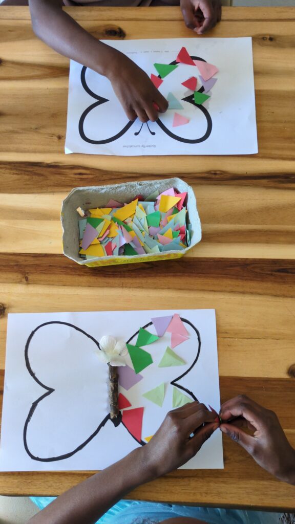 Preschooler spraying water on colored bleeding tissue paper squares inside a hand-drawn butterfly outline for a summer sensory craft.