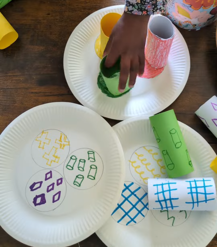 Patterned toilet paper cardboard tubes being stacked into a tower on a paper plate matching game layout for early childhood logical reasoning.