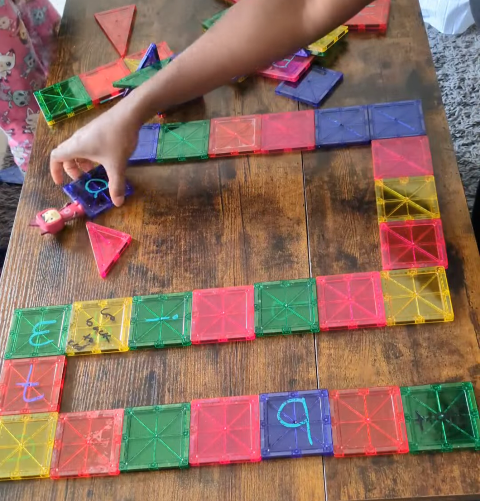 Magna-tiles snapped together on the table with silly action prompts written in dry-erase marker for an interactive family board game.