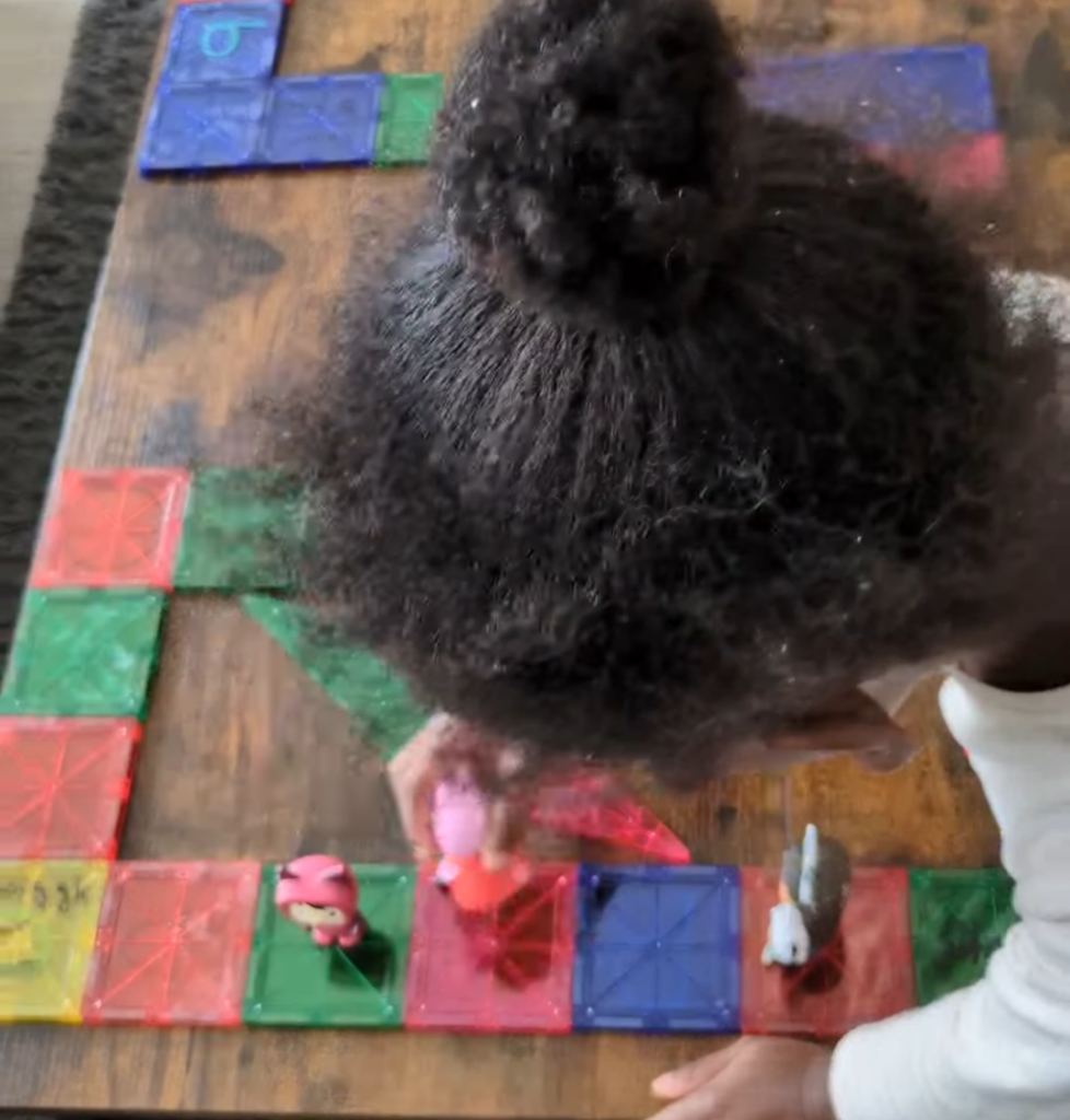 Magna-tiles snapped together on the table with silly action prompts written in dry-erase marker for an interactive family board game.