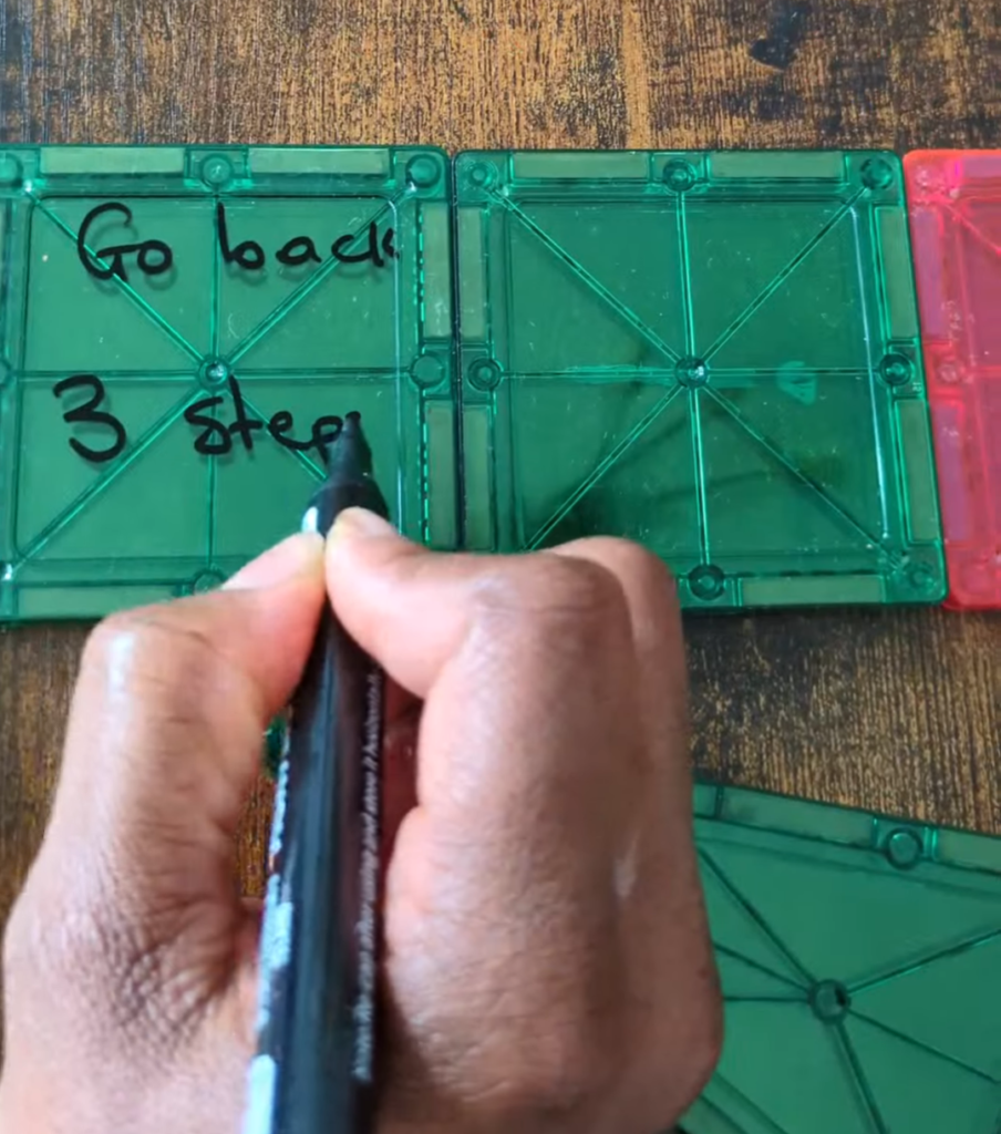 Magna-tiles snapped together on the table with silly action prompts written in dry-erase marker for an interactive family board game.