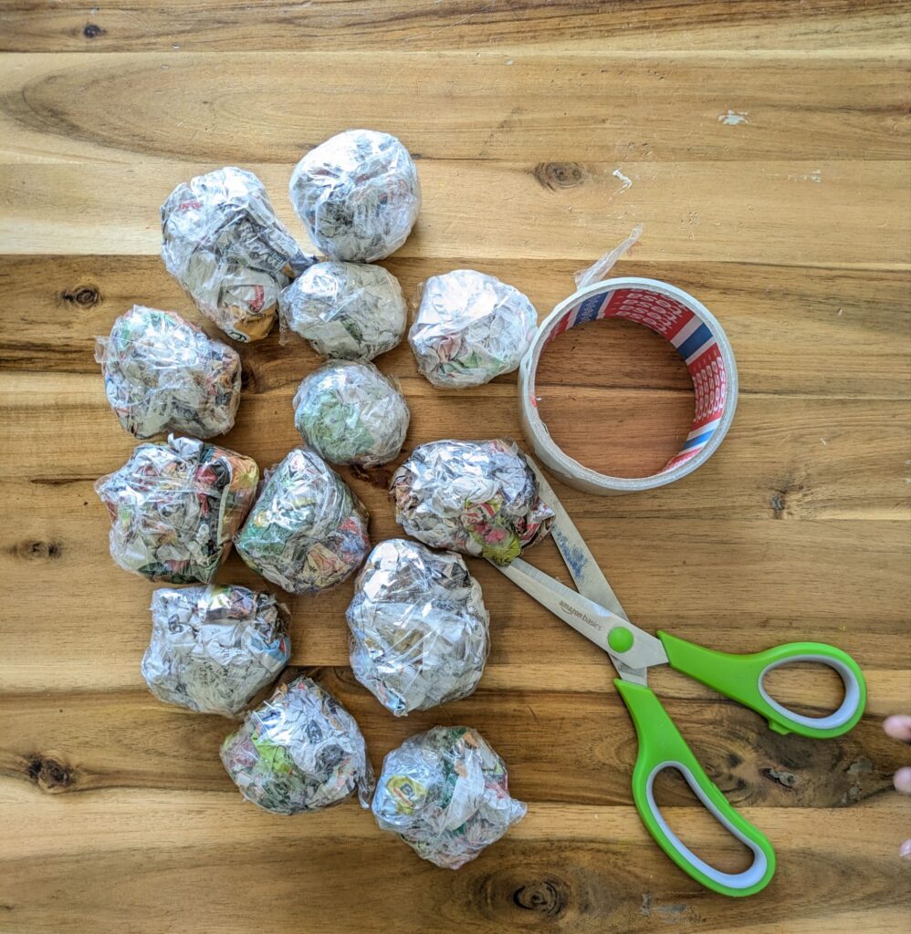 Scrunched-up newspaper balls being thrown through the center openings of cut paper plate hoops taped to a chair for indoor kid energy release.