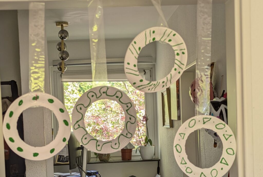 Scrunched-up newspaper balls being thrown through the center openings of cut paper plate hoops taped to a chair for indoor kid energy release.