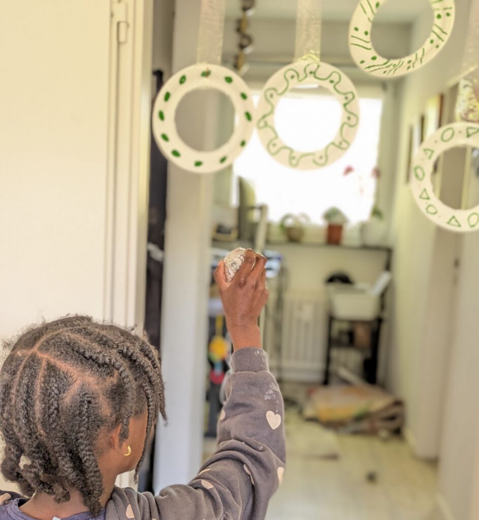 Scrunched-up newspaper balls being thrown through the center openings of cut paper plate hoops taped to a chair for indoor kid energy release.