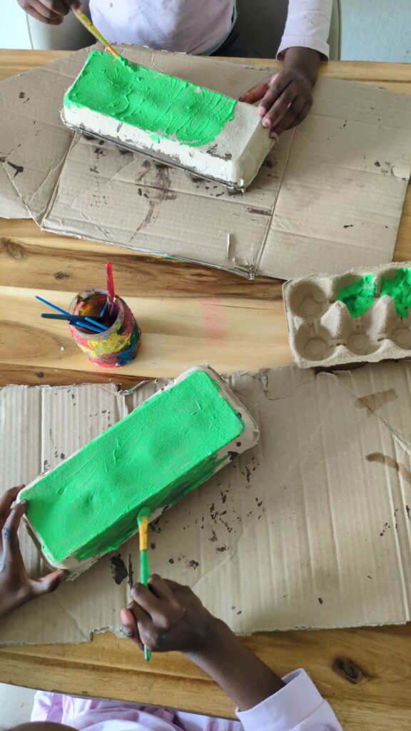 A recycled cardboard egg carton painted brown and green with face-drawn popsicle sticks inserted as worms for a toddler fine motor activity.