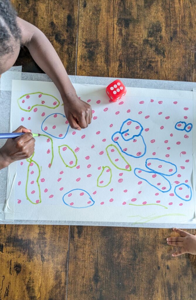 A child rolling a die and circling matching numbers of marker dots on a sheet of paper for a low-prep preschool math game.