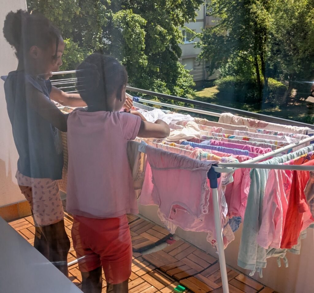 Kids helping hang laundry outside on a balcony in a German apartment, practicing practical life skills.