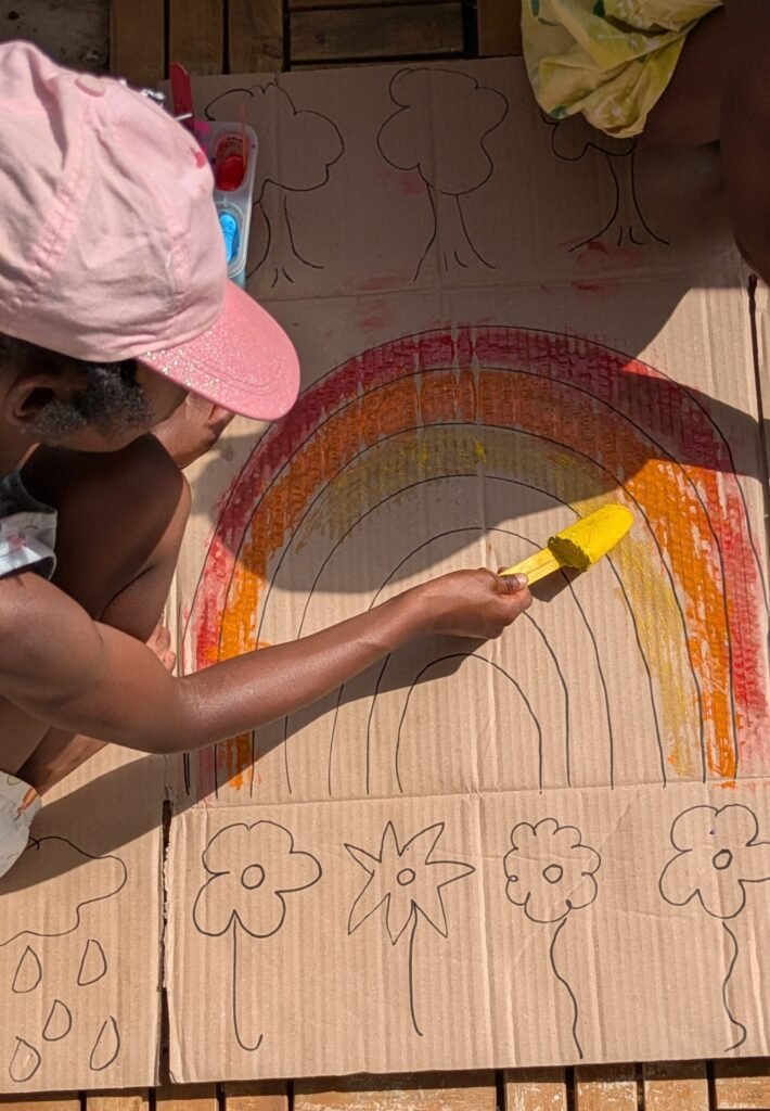Kids painting with frozen popsicle paint on a recycled cardboard box on a small balcony in Germany.